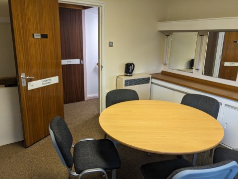 Meeting room with door open to the corridor. A round table can be seen with chairs arranged around it.