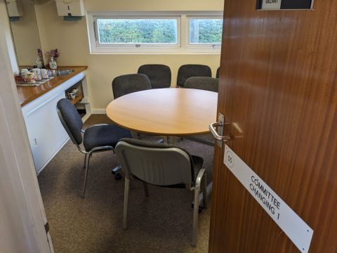 Meeting room with door open into the room from the corridor. A round table can be seen with chairs arranged around it.